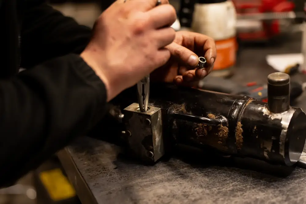 Engineer refitting a component on a worn steel cylinder assembly at a workshop bench